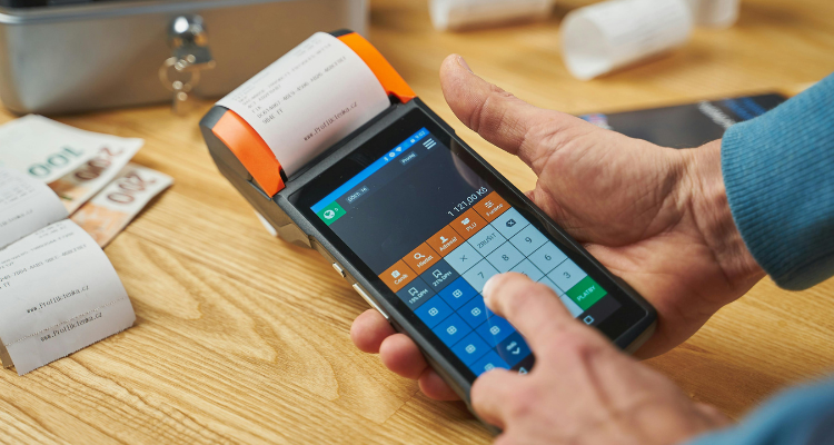 Hand using a portable POS terminal with printed receipt on a wooden desk